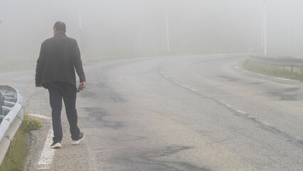 Man from behind walking on a mountain road, in the fog