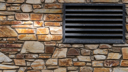 Nice colorful stone wall in beige, orange tones, and black air vent on the right, close up, background