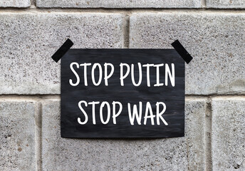 Black poster on gray brick wall. Banner with text STOP PUTIN STOP WAR. RUSSIAN UKRAINIAN WAR....