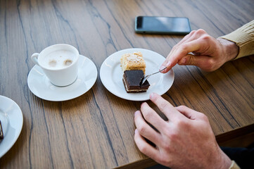Close-up. Hands of a man holding tea spoon and eating delicious chocolate cake at coffee break....