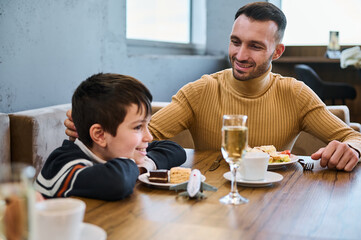 Handsome young man, dad, father stroking son's head while enjoying a healthy meal together in a restaurant