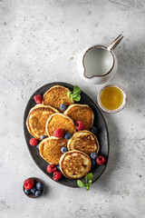 Pancakes with fresh berries and honey on oval plate on gray background, top view