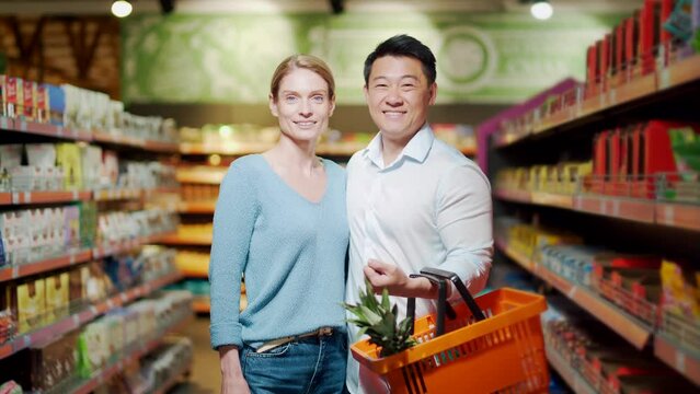 Portrait of a happy asian couple of consumers, supermarket shoppers or grocery store looking at camera smiling. Glad. man and woman together. Close young wife and husband. Family shopping. indoors