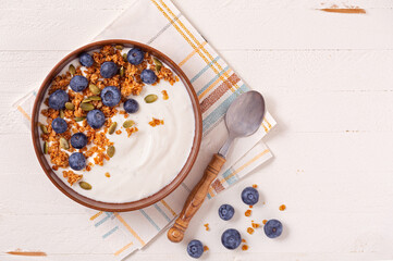 Overhead view of vanilla yogurt with granola and blueberries on a white wooden surface; copy space