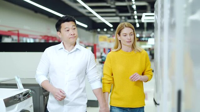 happy mixed race asian couple family man and woman make a choice choose of new household home appliances in supermarket survey Refrigerator Fridge cooler, freezer, cold store purchase and shopping
