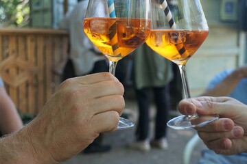Zwei Männerhände mit Weingläsern und gold-braunem Cocktail-Drink stoßen an auf Party im Sommer 
