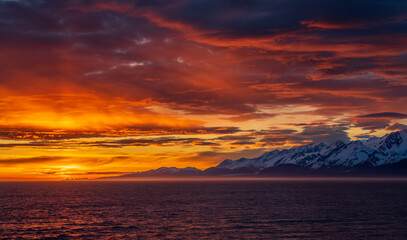 Sun on the horizon by the mountains and Mount Fairweather by Glacier Bay National Park in Alaska