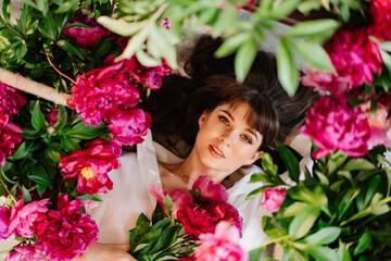a beautiful and gentle young woman lies in peony flowers. feminine beauty. 