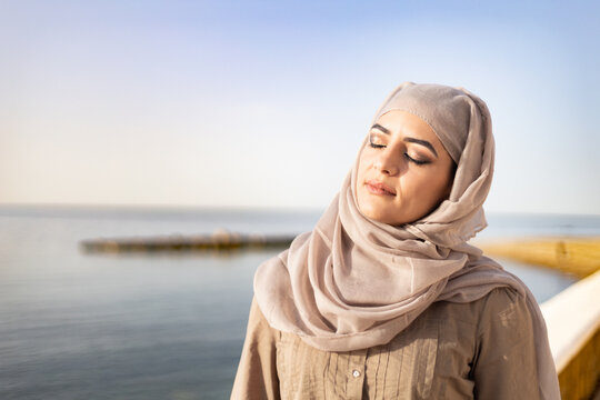 Muslim and modern woman closing eyes on the beach with hope and happiness