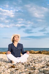 Naklejka na ściany i meble woman wearing a hat meditating on the beach