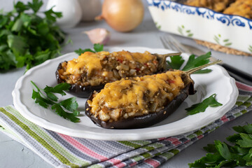 Stuffed eggplant baked with cheese and garlic on a white plate on gray background