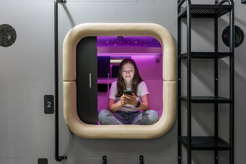 Woman have a rest in capsule hotel with gadget - obrazy, fototapety, plakaty