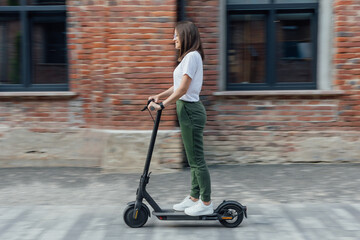 Woman in white t shirt and sneakers rides electric scooter