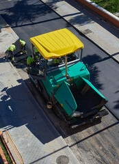 Aerial view of a paver, road paving machine, with a load of new asphalt that will be used to renovate a street. Bitumen and tar used to renew the pavement at roadwork with an asphalt finisher vehicle.