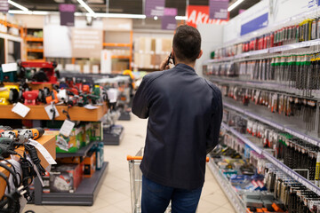 a buyer in a hardware store talking on the phone while walking between the rows of machinery