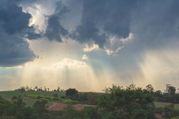 Rural landscape showing greenery, the sky with many clouds and the sun's rays through them