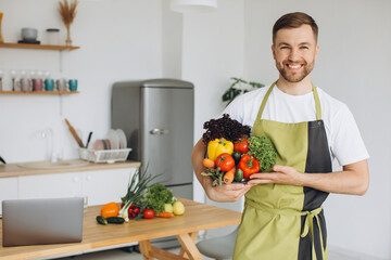 Portrait of a happy man holding a plate of fresh vegetables on the background of the kitchen at home