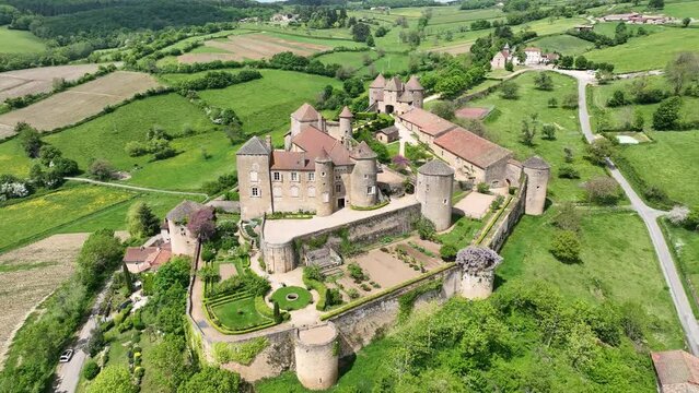 Aerial panning shot of Berze le chatel feudal medieval castle with double enclosure of walls, round towers, donjon, fortified gatehouse on a hill in Central France