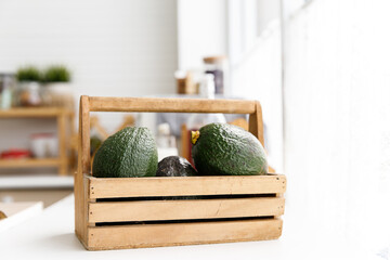 Avocados fruit in wooden basket in the kitchen. Healthy food.