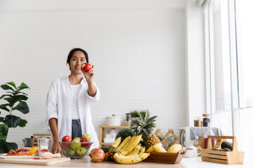 Asian woman holding an apple in the kitchen at home, healthy eating food concept