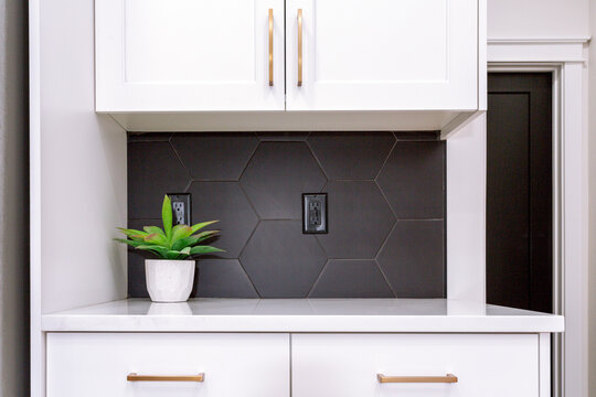 A modern farmhouse kitchen with white cabinets, black hexagon tile backsplash and and gold pulls.