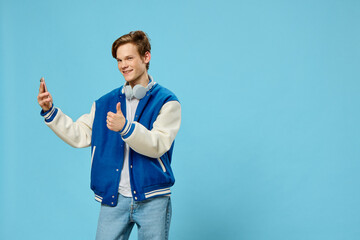 Fototapeta premium handsome stylish young man takes a selfie on the phone with his arm outstretched while standing with headphones around his neck