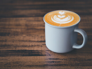 Hot latte coffee with art heart shape in grey ceramic mug on brown wooden table.  .