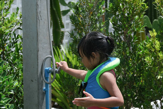 Cute little girl in swimming suits frolicking in the outdoor shower. Happy little girl enjoying in summer day and playing with water.