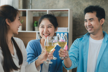 Group of young Asians clinking white wine glasses, startup company parties, New Year's parties, annual company parties, alcoholic beverages. Company employee party catering ideas, celebrations.
