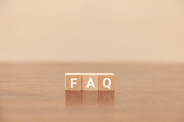 FAQの文字。よくある質問。Frequently Asked Questions。3つの木製ブロックに書かれている。白い文字。木製テーブルと白い壁紙の背景。