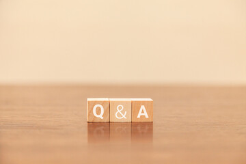 Q&Aの文字。質問と回答。question and answer。3つの木製ブロックに書かれている。白い文字。木製テーブルと白い壁紙の背景。