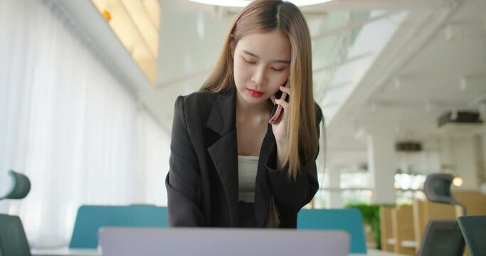 Young busy asian business woman working on project paperwork talking phone, using laptop remotely work in modern office. Female freelancer entrepreneur making distance job telesale call with customer.