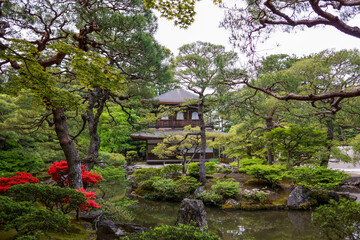 View of Silver Pavilion at Ginkakuji Temple with bonsai trees and pond. Clouds in blue sky background. No people.