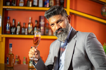 Portrait of happy young beard indian business man holding glass of wine in hand, corporate male celebrate the success of company.