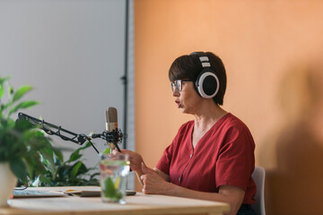 Mature woman making podcast recording for her online show. Attractive business woman using...