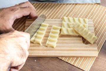 man cutting white chocolate bars and pieces with a knife on a cutting board.