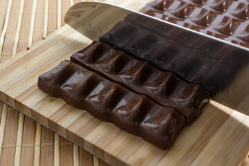 cutting pieces of milk chocolate on a wooden cutting board with a knife