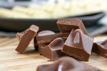 Milk chocolate pieces and chocolate bar on background, over wooden cutting board surface