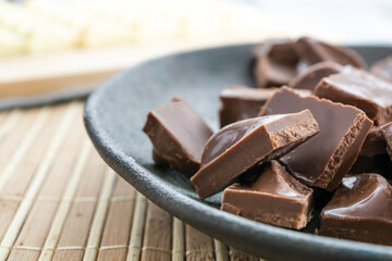 white chocolate bar and chopped pieces of milk chocolate, on a bamboo background and a dark plate