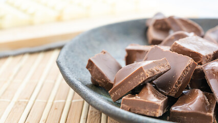 white chocolate bar and chopped pieces of milk chocolate, on a bamboo background and a dark plate