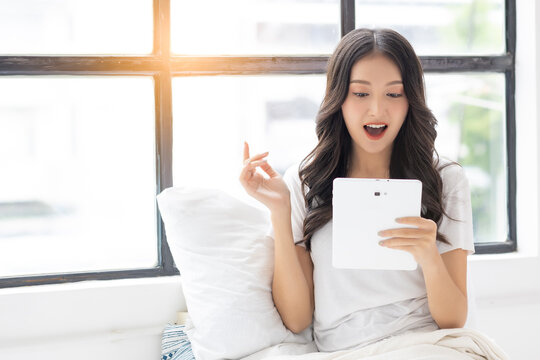 Young happy surprised shocked using tablet computer Using internet online on tablet pc Lifestyle beautiful Asian girl relaxing smiling enjoying at home Facial expression excited woman with great news