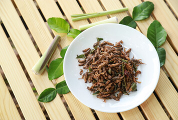 spicy fried cricket with herbal leaf on wooden table for eating