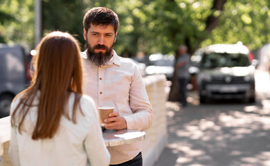 Obraz premium Romantic young couple drinking coffee outdoors while standing at a table in a street cafe, man and woman enjoying a relaxing conversation