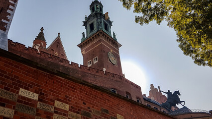 Obraz premium A view on the tall bell tower of Wawel Castle in Cracow, Poland. There is a high defence wall around the castle. A monument of Tadeusz Kosciuszko riding a horse in the back. Clear and bright day.