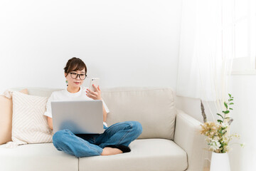 Fototapeta premium 家のソファでパソコンとスマホを見る日本人女性（真剣・共有・連携） 