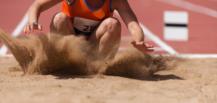 Female athlete long jump landing sand spray, landing in long jump in track and field