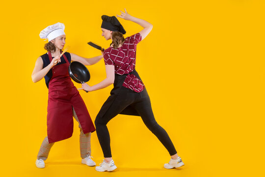 Battle of chefs. Woman cooks are fighting. Cooking competition concept. Women with frying pans attack each other. Cook girls on yellow. Battle of restaurant employees. Chef woman's fight