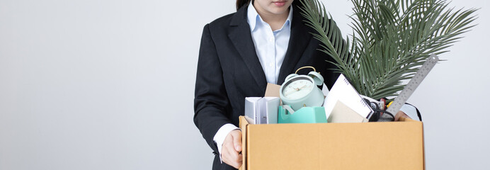 Businesswoman wearing a black suit raises a brown cardboard box from the office, Businessmen pack personal belongings and equipment after Resign or being fired, Employment contract is expired.