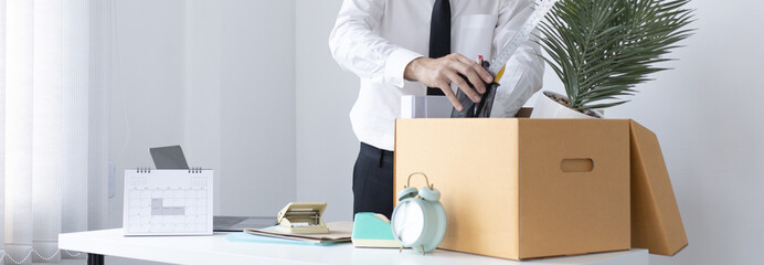 Put the work equipment in the office in a large brown box, Businessmen are keeping work documents and personal belongings due to resignation or being fired, termination of employment. - obrazy, fototapety, plakaty