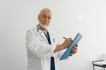 Professional doctor taking notes on clipboard and looking camera in medicine center